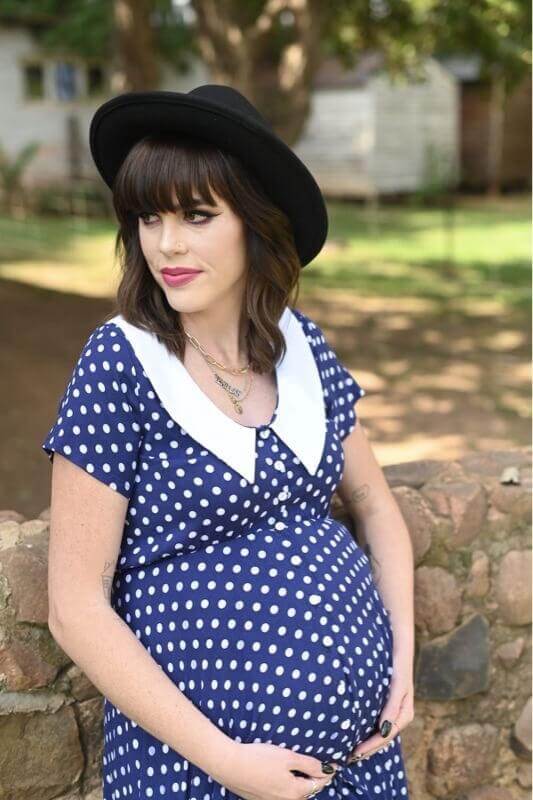 Navy and white polka dot maternity and nursing dress with Peter Pan collar, short sleeves, and hi-low silhouette