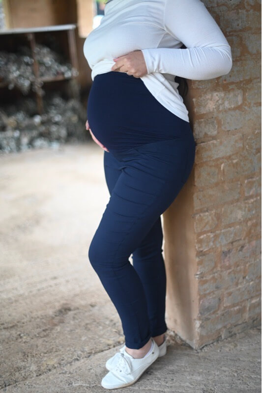 Pregnant woman wearing navy skinny maternity pants with stretchy belly band